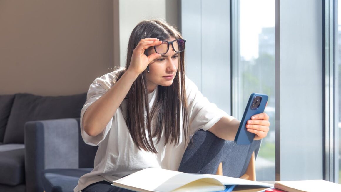Jovem usando celular e notebook com sintomas de fadiga ocular